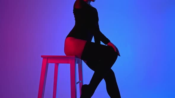 Professional Ballet Dancer in Hat Sitting on High Chair on Multicolored Background Under Violet and