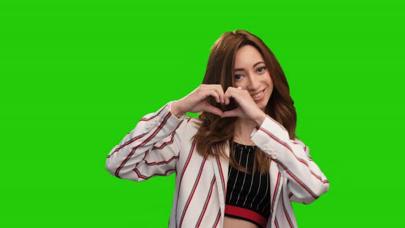 Adorable young woman posing on green screen showing heart and thumb up gestures