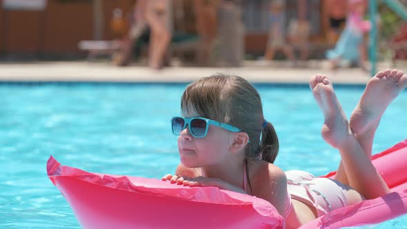 Happy Child Girl Relaxing on Inflatable Air Mattress in Swimming Pool on Sunny Summer Day During