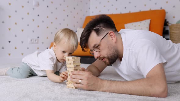 Dad and Toddler Son Playing Together and Building a Wooden Blocks Tower at Home