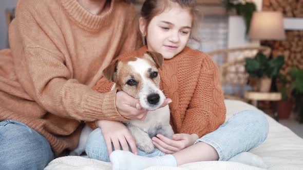 Young Mother Daughter in Knitted Sweaters are Sitting on a Bed in a Cozy Bedroom with Their Small