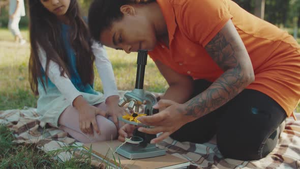Teacher Tuning Microscope Showing Nature Object to Girls Outdoors