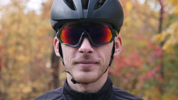 Attractive caucasian professional cyclist looking to camera and taking off sport glasses after ride