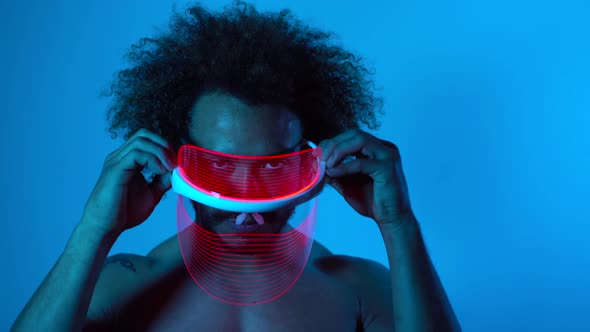 Man wearing light therapy mask against blue wall