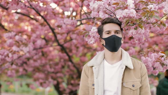 Pandemic, portrait of a young man on a woolen jacket on black virus protective mask on street. 