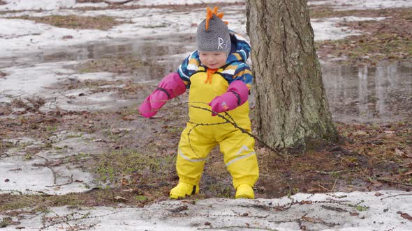 Cute Child in Yellow Waterproof Rain Pants Bibs for Kids and Rubber Boots on a Walk in Park in Early