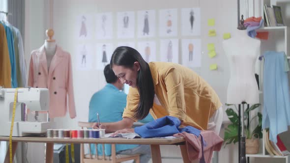Asian Female Drawing Clothes On The Paper While Male Designing Clothes On The Desktop In The Studio