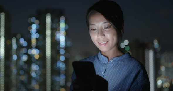 Woman look at cellphone with the building background at night