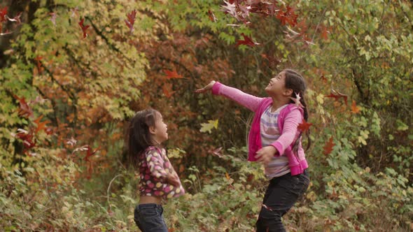 Two young girls in Fall throwing pile of leaves