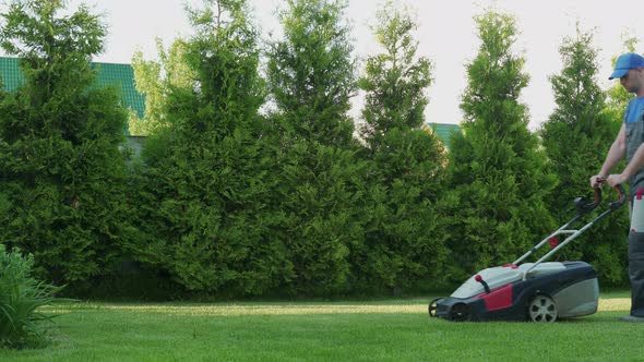 Young Gardener in Overalls Uses a Lawn Mower on the Plot