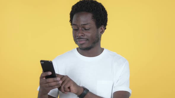 African Man Browsing Smartphone Yellow Background