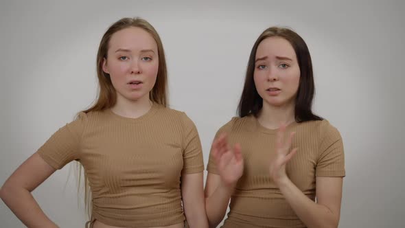 Identical Twin Sisters Arguing Gesturing Talking Blaming Each Other Looking at Camera