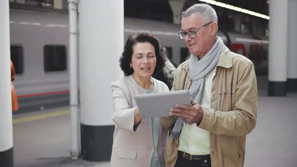 Senior Couple Ready To Go on Vacation Using Digital Tablet Standing on Railway Platform