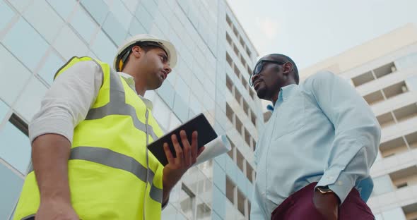 Low Angle View of African Inspector and Indian Foreman with Tablet Shaking Hands Outdoors