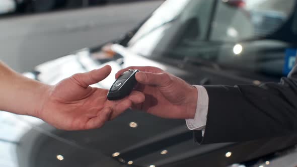 Male Hand Gives a Car Keys To Man Hand in the Car Dealership Close Up. Unrecognized Auto Seller and