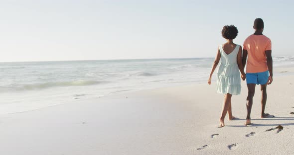 African american couple holding hands and walking on sunny beach