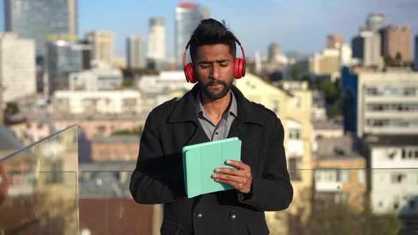 Medium Shot Portrait of Joyful Middle Eastern Man Turning on Playlist on Tablet Dancing in Sunshine