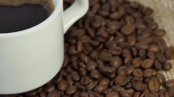 White Cup with Coffee on the Background of Fresh Roasted Coffee Beans