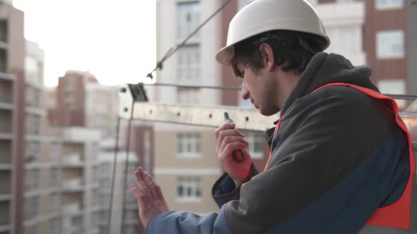 A construction engineer at a construction site controls a crane using a radio walkie-talkie.