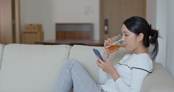 Woman look at cellphone with cup of tea, relax at home