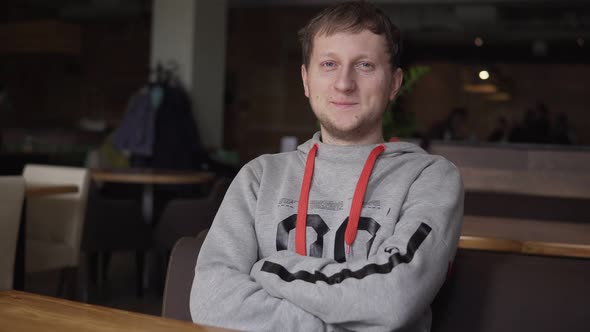 Handsome Young Man Smiling Into the Camera Sittin at the Table in Restaurant