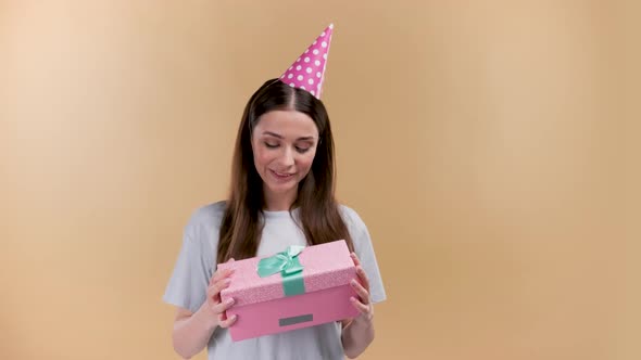 Happy Young Cheerful Birthday Girl with a Present Wearing Party Head on a Beige Background