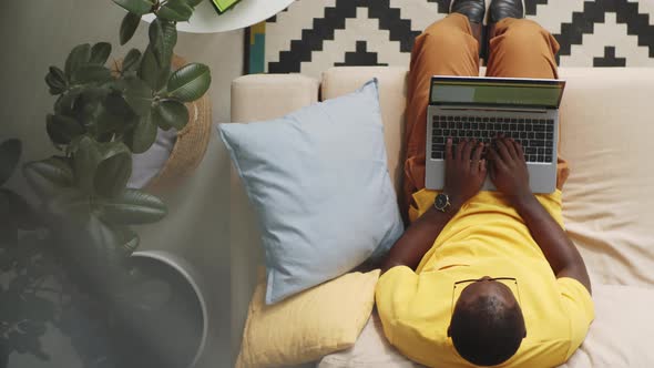 Afro-American Man Sitting on Sofa and Typing on Laptop