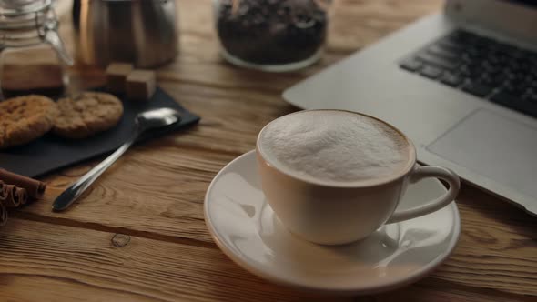 Woman Puts a Cup of Coffee on the Table with a Laptop