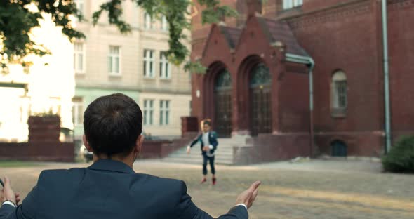 Backside View of Man in Suit Waiting for His Kid After Lessons Near School Building. Cheerful Boy