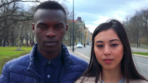 A Young Black Man and a Young Asian Woman Look at the Camera in a Street in an Urban Area