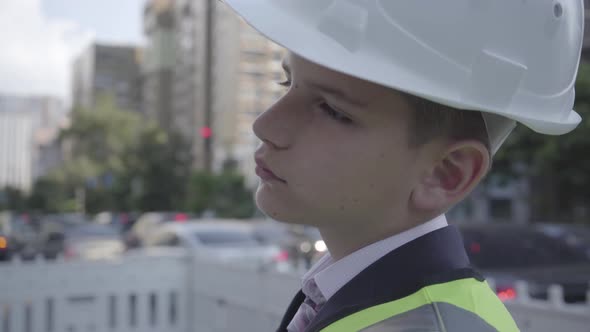 Cute Little Pensive Boy Wearing Business Suit and Safety Equipment and Constructor Helmet Standing