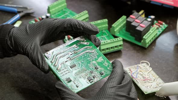 Professional master in black gloves examines electrical board in hands for repair. Close-up.