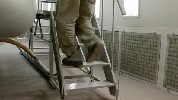 Man Climbs Stairs Next to Helicopter to Be Painted in Spray Booth