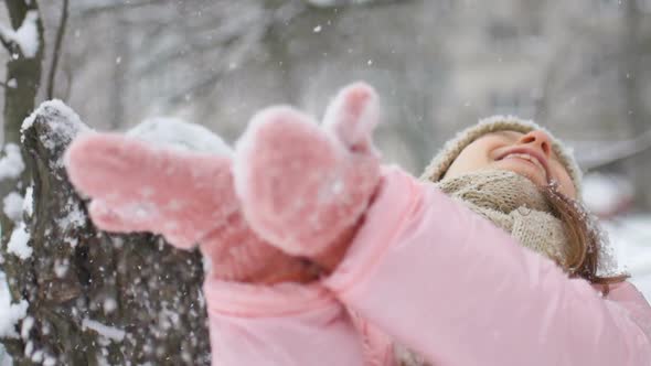 Winter Portrait of a Kid Girl in Pink Coat Wearing Beige Hat and Mittens Playing Outdoor in Snowy