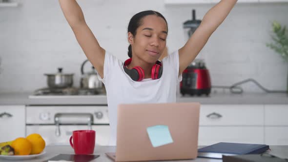 Satisfied Young Slim Woman Stretching in the Morning Sitting at Kitchen Table with Laptop Smiling