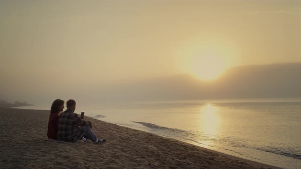 Couple Sitting on Beach at Sunset