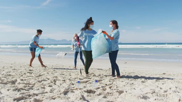 Diverse group of women wearing volunteer t shirts and face masks picking up rubbish from beach