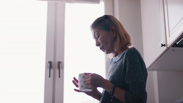 Lonely Senior Woman Drinking Hot Tea and in the Kitchen