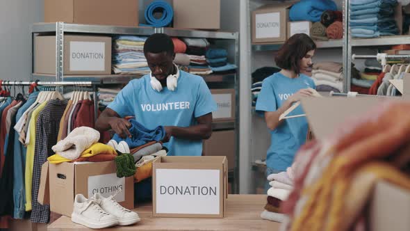 Diverse Male and Female Volunteers Sorting Clothes and Putting It Into the Cupboard Box at the