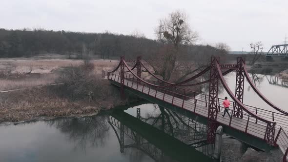 Woman is running on bridge across river, aerial drone view.