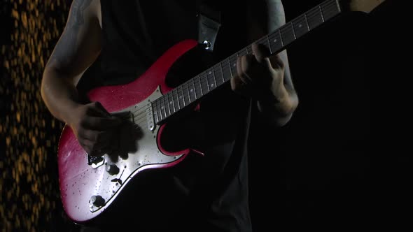 Rock Musician Plays a Red White Electric Guitar in a Dark Studio Against the Background of Falling