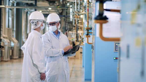 Two Specialists in Lab Coats are Operating Factory Equipment