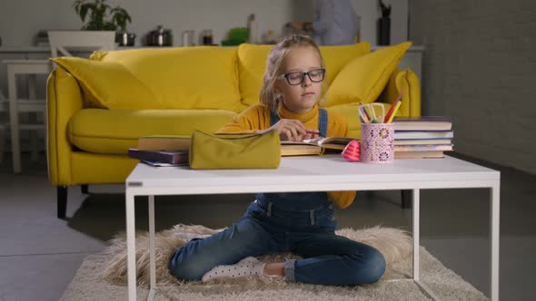 Cute Schoolgirl Studying with Book at Coffee Table