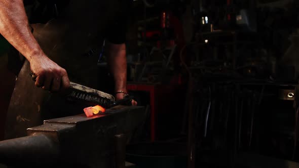 Mid-section of blacksmith using wire brush on hot iron