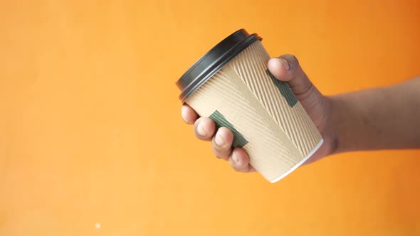 Hand Holding Take Away Paper Cup Against Orange Background