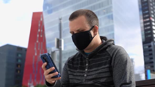 Man Using Smartphone Wearing Mask on Bench