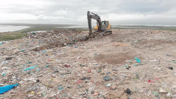 Digger clearing rubbish piled on a landfill full of trash