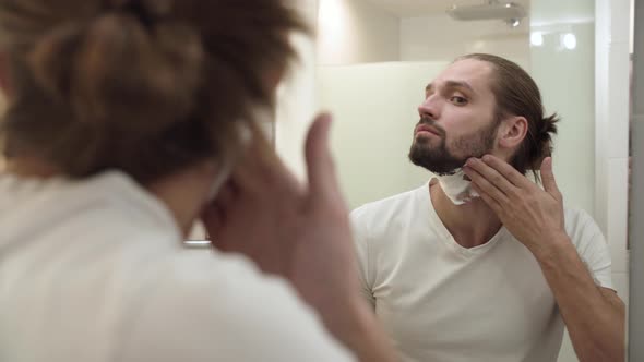 Man Applying Shaving Foam On Face Skin And Looking In Mirror