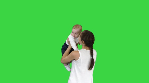 Young Mama Playing with Baby By Rising Him Up on a Green Screen, Chroma Key.