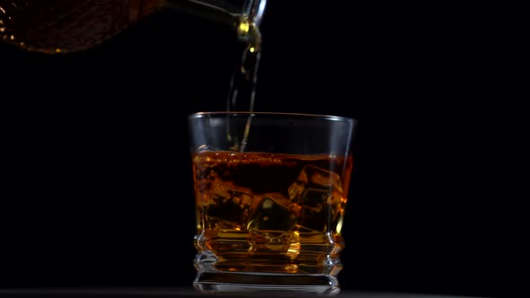 Golden Whiskey in Faceted Glass with Ice Cubes Rotating on Black Background Macro